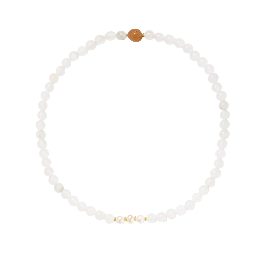 Three layered white beaded bracelets with carved orange agate lotus centerpiece and freshwater pearls on cream background.
