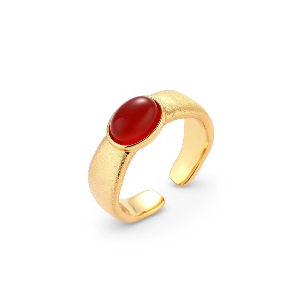 Close-up of brushed gold-plated ring with deep red oval stone, featuring adjustable band design on neutral background.