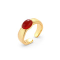 Close-up of brushed gold-plated ring with deep red oval stone, featuring adjustable band design on neutral background.